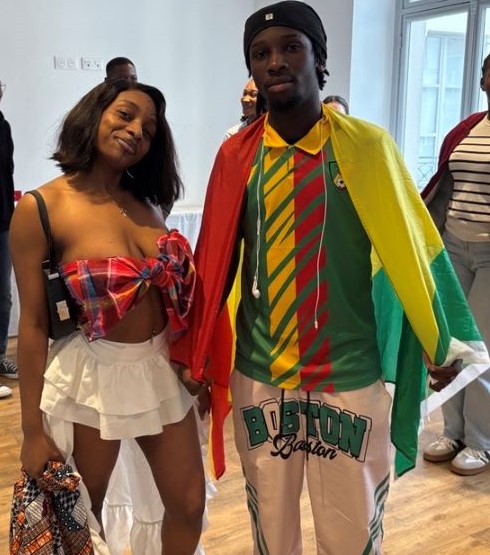 Une étudiante habillée en tenue traditionnelle debout à coté d'un étudiant portant un maillot et un drapeau de son pays.